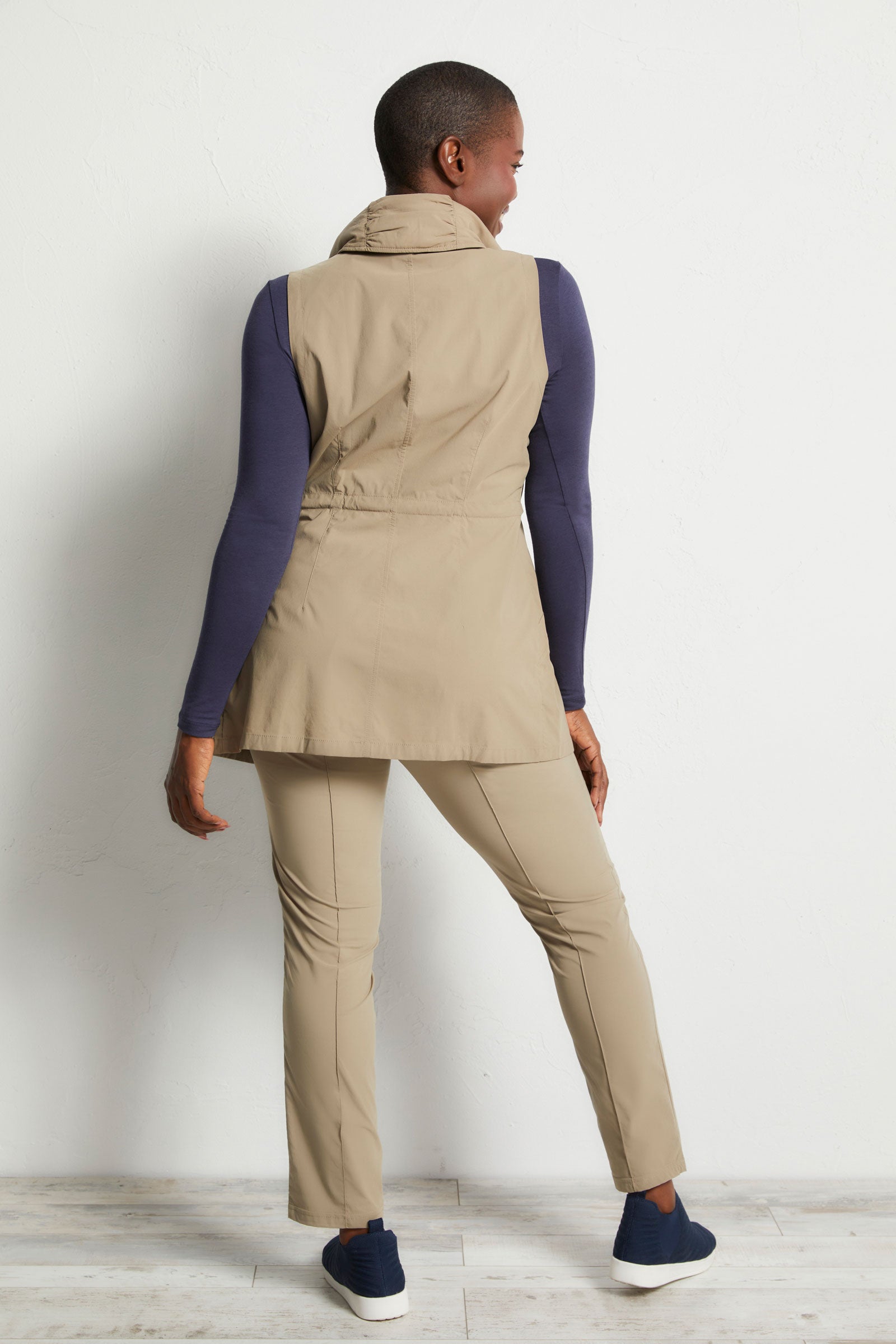 The Best Travel Vest. Woman Showing the Back Profile of a Delaney Travel Vest in Khaki.