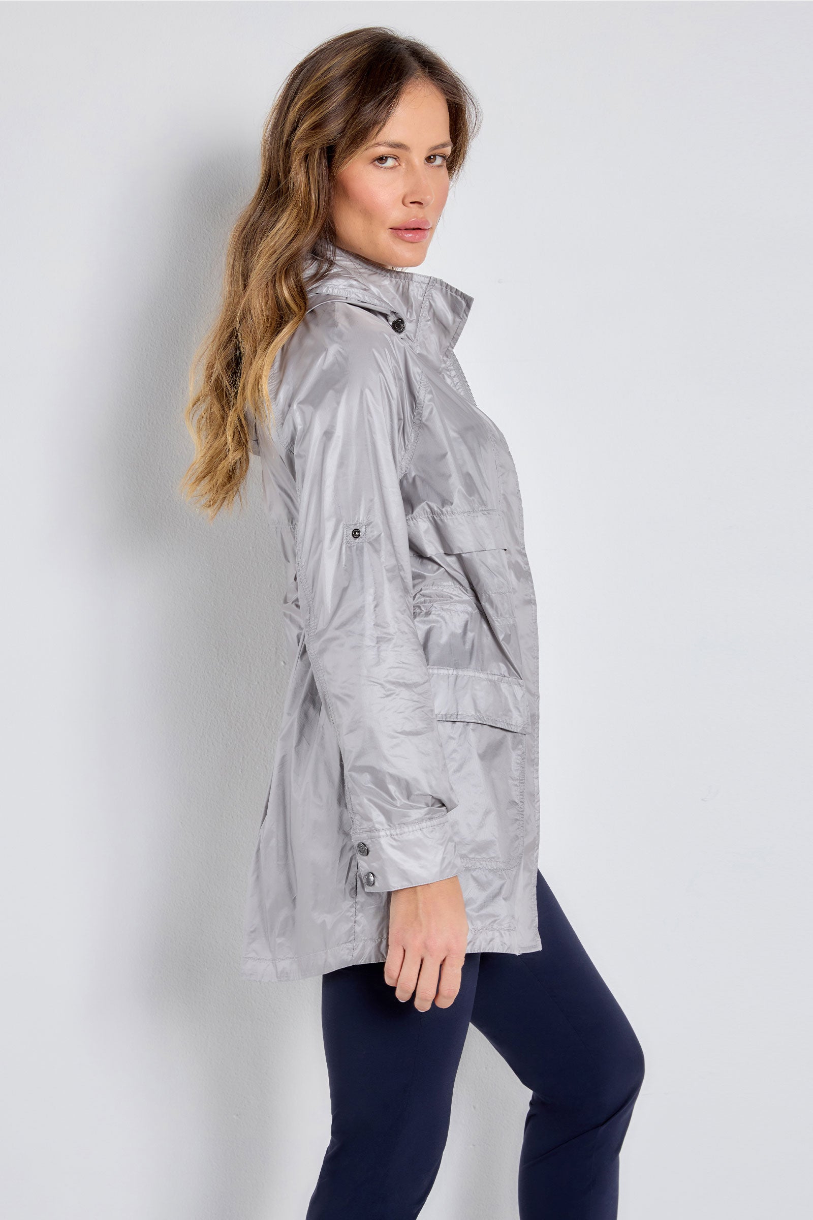 The Best Travel Jacket. Woman Showing the Side Profile of a Ramona Windbreaker Jacket in Silver Grey.